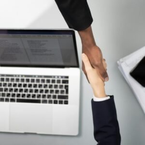 Work With Me Overhead view of a professional handshake over a laptop, symbolizing business agreement.